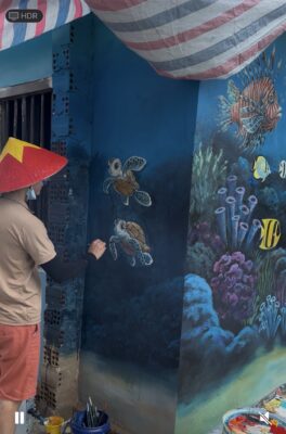 Họa sĩ đang vẽ rùa biển và cá trên tường xanh ngoài trời