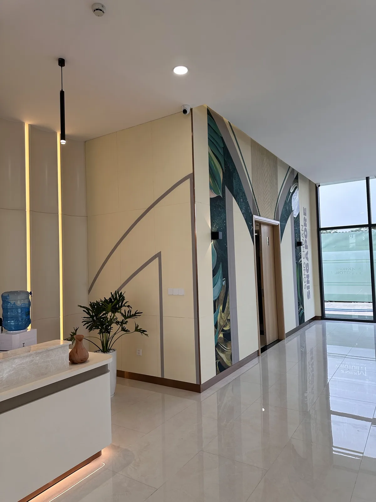 Tranh tường nhà mẫu nhìn từ quầy lễ tân, mảng lá nhiệt đới nối liền hai mặt tường