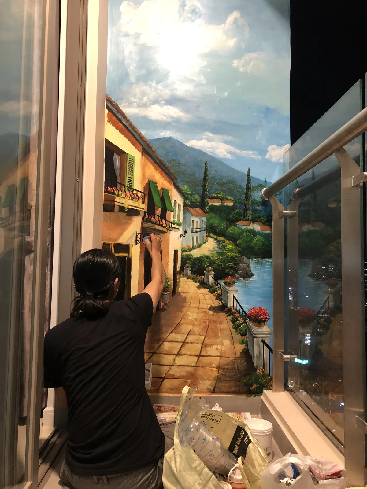 Họa sĩ đang vẽ tranh tường 3D hẻm phố châu Âu ban công hoa dẫn ra hồ