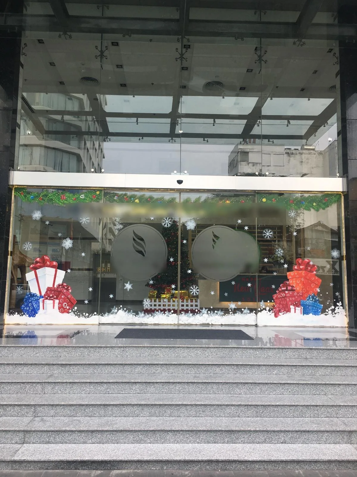 Vẽ tranh kính Noel hộp quà đỏ, trắng, xanh và bông tuyết trên cửa kính sảnh văn phòng