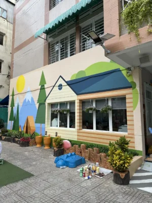 Vẽ tranh tường trường mầm non: mặt tiền ngôi nhà mái xanh, núi và rặng thông